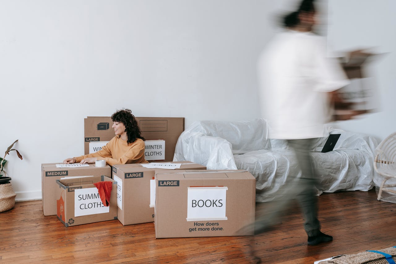 about-02 A couple packing labeled boxes in a minimalist living room, preparing for moving day.